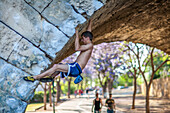 Young climber practicing free climbing under the iconic Triana Bridge in Sevilla, Andalusia, Spain. Displaying strength and determination.