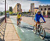 Zwei Radfahrer fahren an einem sonnigen Tag durch das Ramon y Cajal-Viertel in Sevilla, Andalusien, Spanien, und genießen die urbane Landschaft der Stadt.