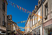 Vibrant red and yellow flags hanging across a charming street in Guerande, France on a sunny day.