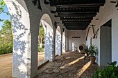 Sonnenbeschienener gewölbter Korridor mit weißen Wänden und Steinboden im Palacio Ducal de Medina Sidonia in Sanlucar de Barrameda, Andalusien, Spanien.