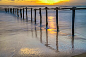 Atemberaubender Sonnenuntergang über einem ruhigen Strand mit einem Holzzaun, der die Grenze des Nationalparks Donana in Matalascanas, Almonte, Huelva, Andalusien, Spanien, markiert.