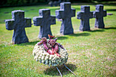 Eine düstere Szene auf dem deutschen Soldatenfriedhof in der Normandie, Frankreich, mit einem Gedenkkranz und Steinkreuzen.