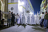 Nazarenos from the Resurrected Brotherhood during Easter Sunday morning procession in Seville, Spain. Nighttime religious tradition with spectators watching.