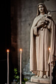 Three lit candles in front of a statue inside Coll giale Saint-Aubin, Guerande, France, creating a serene and spiritual atmosphere.