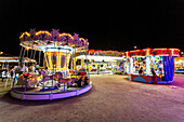 Illuminated children's rides on the beach at night in Sanlucar de Barrameda, Andalusia, Spain. A vibrant and fun atmosphere for families and friends.