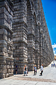 Besucher erkunden das historische römische Aquädukt in Segovia, Castilla y Leon, Spanien, an einem strahlenden Sonnentag.