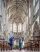 Photograph of the grand interior of Eglise Saint Pierre in Caen, Normandy, France, featuring beautiful Gothic architecture and two people admiring the structure.