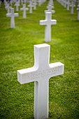 White cross for an unkown soldier at the American military cemetery in Normandy, France, honoring fallen soldiers with rows of graves on green grass.