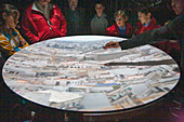 Visitors examine an image of downtown Sevilla projected inside a camera obscura exhibit, appreciating the detailed cityscape.