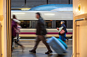 Unscharfe Bewegung von Passagieren mit Gepäck auf dem Bahnsteig des Bahnhofs Santa Justa in Sevilla, Spanien. AVE-Zug im Hintergrund.