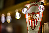 A blurred image of a Sevilla FC banner illuminated by festive string lights. Ideal for celebration and sports-themed visuals.