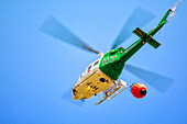 Aerial view of a firefighting helicopter carrying a water bucket over Fuenteheridos, Huelva, Andalusia, Spain on a clear day.