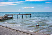 Ruhiger Tag am Omaha Beach in der Normandie, Frankreich, mit einem ruhigen Pier und einem kleinen Boot, das auf sanften Wellen schwimmt.