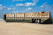 Tourists visit the remains of Mulberry B artifact on Gold Beach in Arromanches, Normandy, France, showcasing history and legacy of World War II.