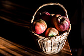 A wicker basket filled with fresh, red apples placed on a rustic wooden surface. Captured in Fuenteheridos, a charming village in Huelva, Andalucia.