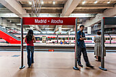 Madrid Atocha Station in Madrid, Spain, showcasing passengers waiting for a commuter train amidst modern architecture.