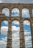 Stunning view of the ancient Roman aqueduct in Segovia, Spain, with arches framed by a clear blue sky and scattered clouds.