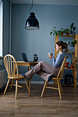 Frau mit Tasse in der Hand und Blick auf den Laptop zu Hause