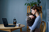 Woman holding cat and looking at laptop at home