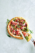 Pizza with prosciutto, rocket, onions and olives