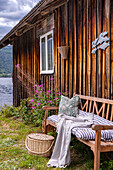 Wooden bench with striped seat cushion in front of rustic cabin by the lake