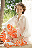 Brunette woman in cream-coloured blouse and orange-patterned trousers