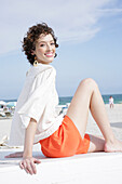 Brunette woman in cream-coloured blouse and orange shorts