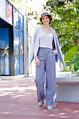 Young woman in casual business outfit walking outside with straw hat