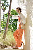 Woman in striped orange and white summer clothing in front of palm trees