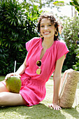 Young woman in pink, short jumpsuit with cocktail in coconut