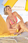 Woman in striped bikini applying sun cream on the beach