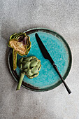 Halved raw artichoke and knife on a turquoise plate