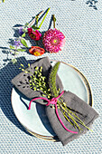Grauer Leinenserviette mit Wildblumen auf Keramikteller, gemusterte Tischdecke
