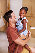 Father carrying smiling daughter at home