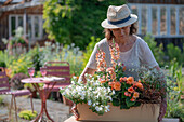 Frau trägt Blumenkasten mit Löwenmäulchen (Antirrhinum Majus), Begonie (Begonia), Mahagonigras 'Everflame', Zauberglöckchen (Calibrachoa), Zauberschnee