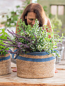 Frau hinter Korb mit Duftkräutern, Thai-Basilikum, Pfefferoregano, Zitronenverbene, Heilminze und Bergminze (Calamintha nepeta) in Basttasche