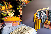 Bedroom with floral wallpaper and colourful clothes on wardrobe rail