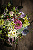 Rustikales Blumengesteck mit Chrysanthemen (Chrysanthemum) und Disteln auf Holztisch