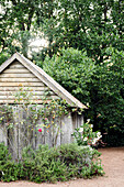 Wooden hut in the garden surrounded by lush greenery and flowers