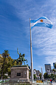 A large Argentine flag flies over the statue of General Manual Belgrano in the Plaza de Mayo on a cloudy day in Buenos Aires, Argentina.