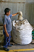 Ein Arbeiter mit einem Sack roher, ungereinigter Schafswolle in der Hilandería Warmi, einer Weberei in Palpalá, Argentinien