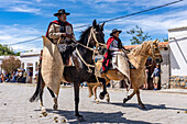 Gauchos in traditional outfits riding on horseback in a parade in Cachi, Argentina. Cowhide guardemontes protect the rider from thorn bushes common in the area.