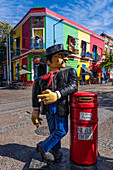 A caricature statue of a man leaning on a mailbox while smoking in Caminito, La Boca, Buenos Aires, Argentina. On the balconies behind are statues of Diego Maradona.