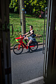 Young woman riding Lime rental bike in Prague, viewed from tram door