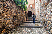 A young woman ascends a stone stairway surrounded by historic walls in Yanguas.