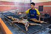 A cook grills meat over coals in a traditional parrilla in Termas de Rio Hondo, Argentina.