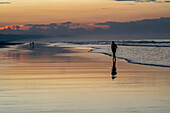 Sunset on the beach in Las Lajas, Panama. People walk on the beach silhouetted.