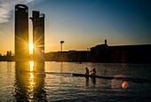 Two rowers glide through the Guadalquivir River during a stunning sunset in Seville, Spain. The scene captures the beauty and tranquility of the evening waterside.