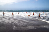 A group of bathers enjoying the waves at Bollullo Beach on the northern coast of Tenerife, La Orotava, Canary Islands, Spain. Long exposure.