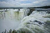 The water of the Iguazu River falls over the precipice of the Garganta del Diablo or the Devil's Throat Waterfall in Iguazu Falls National Park in both Argentina and Brazil. Both parks are UNESCO World Heritage Sites. At left is Brazil, at right is Argentina.